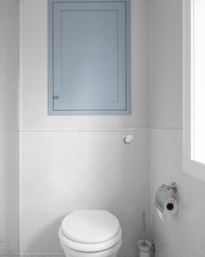 Toalett i klassisk stil på bad med marmorflis på gulv, innegbygd skap for ekstra oppbevaring over.