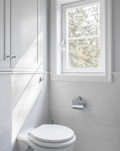 Toalett på bad i klassisk stil med metroflis på vegg og brystning. Innebygde skap over toalettet.