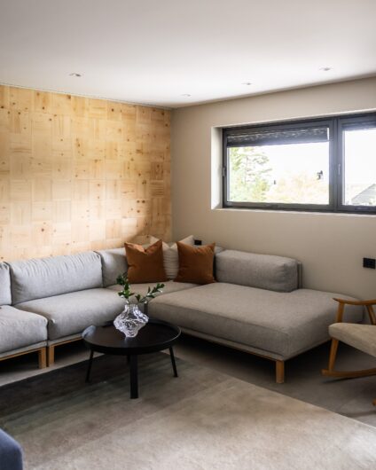 TV stue med tapet på vegg av trevirke. Lys sofa i skandinavisk stil. Utført av Lomundal.